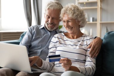 Gülümseyen 60 'ların çifti kredi kartıyla online alışveriş yapıyor.