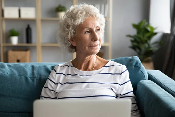Pensive reife Frau entspannen mit Laptop zu Hause denken — Stockfoto