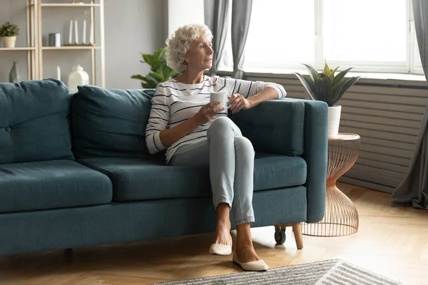 Calm mature woman relax on couch drinking tea — Stock Photo, Image