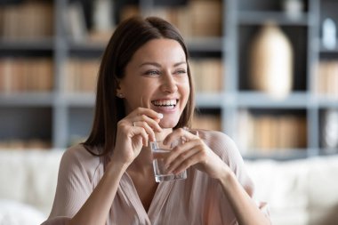 Smiling young woman holding pill and glass of pure water. clipart