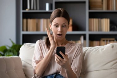 Şok olmuş genç esmer kadın akıllı telefon ekranına bakıyor..