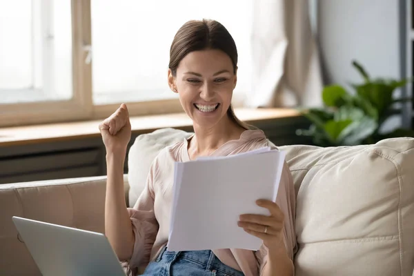 Excited young woman reading paper documents, making yes gesture.
