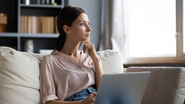 Distraherad från arbetet ung kvinna sitter på soffan med bärbar dator. — Stockfoto