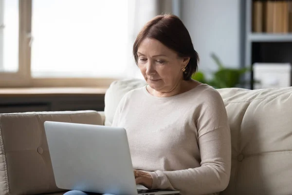 Konzentrierte Frau mittleren Alters chattet in sozialen Netzwerken mit Freunden. — Stockfoto