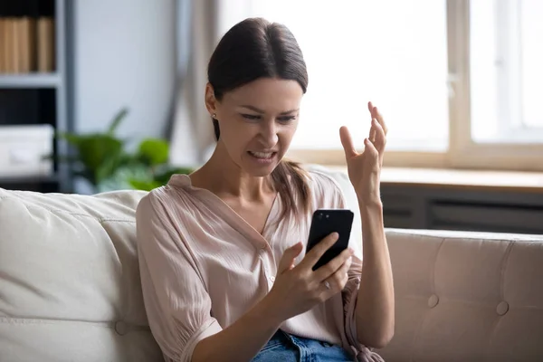 Wkurzona młoda kobieta patrzy na ekran telefonu komórkowego. — Zdjęcie stockowe