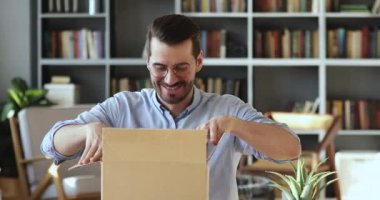 Smiling young man customer opening parcel box sitting at desk