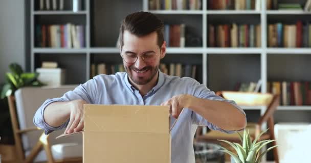 Smiling young man customer opening parcel box sitting at desk — Αρχείο Βίντεο