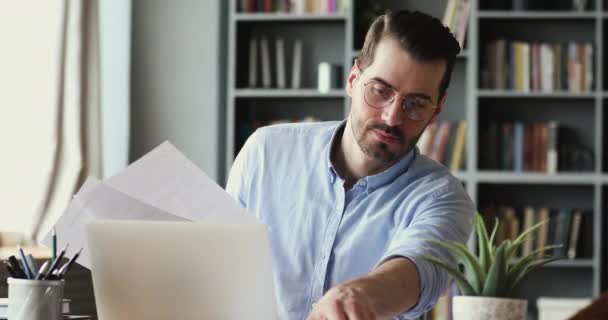 Serious young businessman checking corporate paperwork sitting at desk — ストック動画