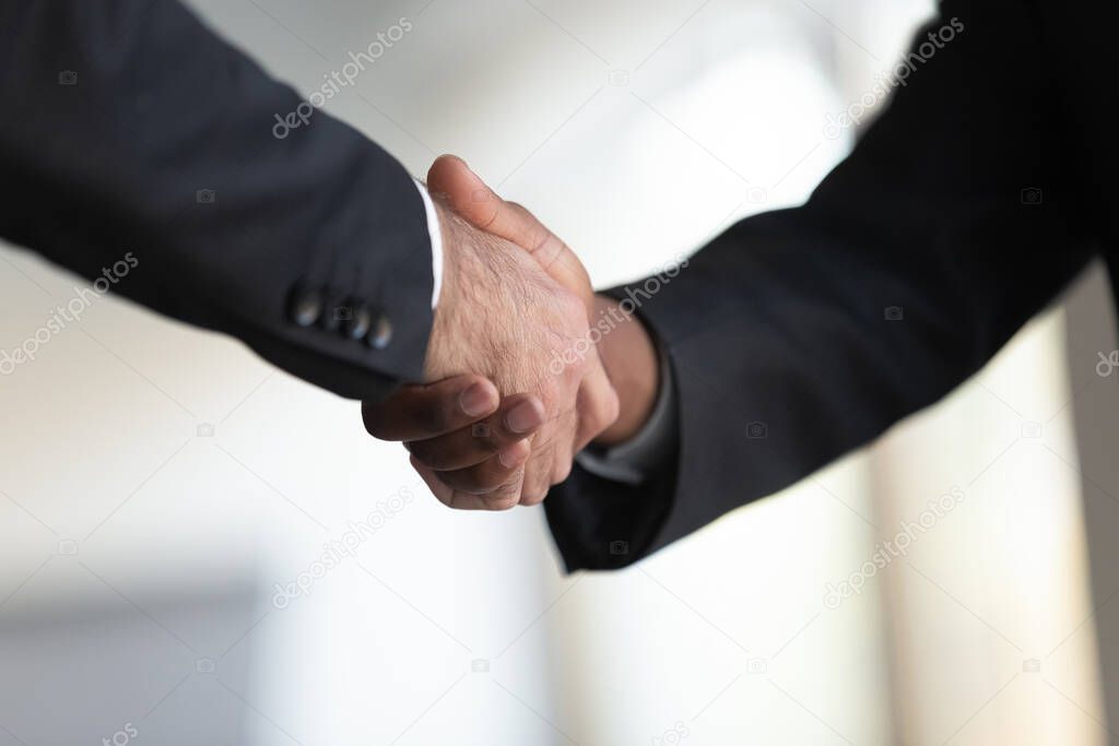 Two mixed race businessmen in suits shaking hands at office.