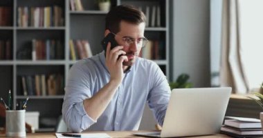 Smiling business man using laptop talking on phone in office