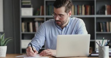 Focused business man working on laptop computer making notes