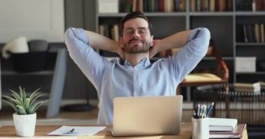 Satisfied employee relaxing at office desk holding hands behind head
