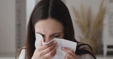 Ill allergic young woman sneezing in tissue blowing running nose