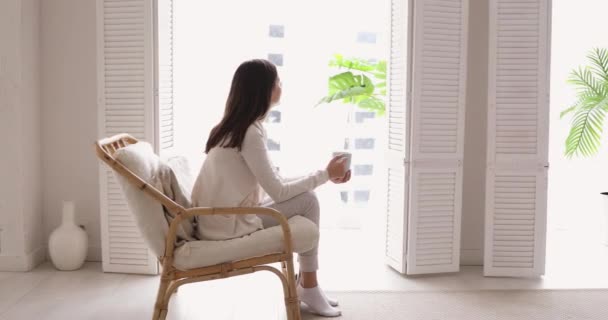 Relaxed young woman drinking tea looking through window in apartment — 图库视频影像
