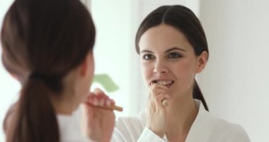 Happy woman holding wooden toothbrush brushing teeth looking in mirror