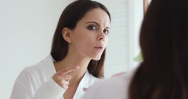 Upset girl worried about facial skin problem looking in mirror