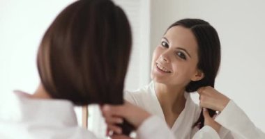 Smiling young beautiful woman touching healthy hair looking in mirror
