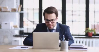 Excited male executive wearing suit feeling overjoyed looking at laptop