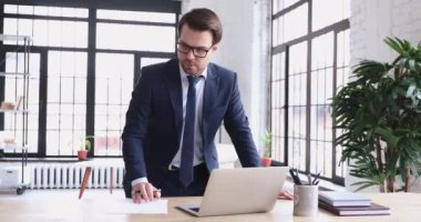 Serious male ceo working in office using laptop making notes