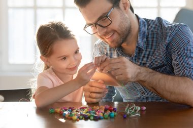 Gülümseyen genç baba küçük anaokulu kızına bilezik yapmasında yardım ediyor..