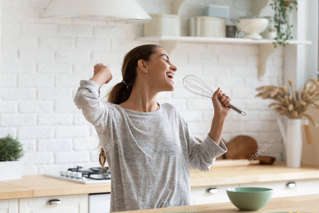 Excited funny girl singing into whisk, having fun in kitchen