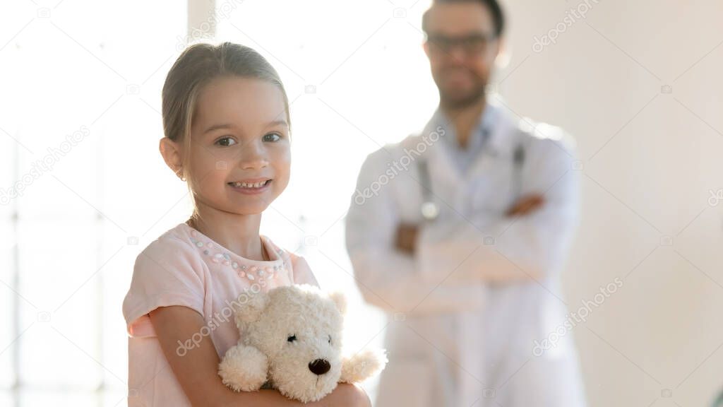 Portrait of little patient with pleasant male doctor on background.