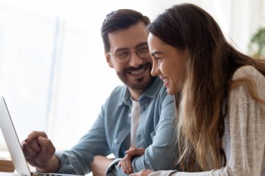 Mutlu çift birlikte dizüstü bilgisayar kullanıyor, el ele tutuşuyorlar.