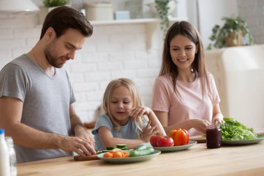 Küçük kızıyla birlikte yemek pişiren mutlu genç ebeveynler.