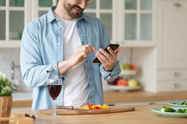 Gülümseyen adam akıllı telefon kullanıyor, salata pişiriyor, sebze hazırlıyor.