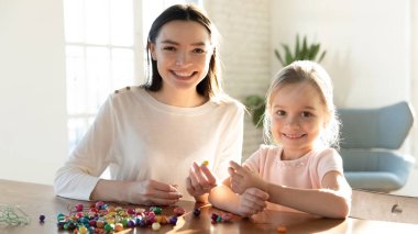 Smiling young mother creating handmade bracelets with daughter. clipart