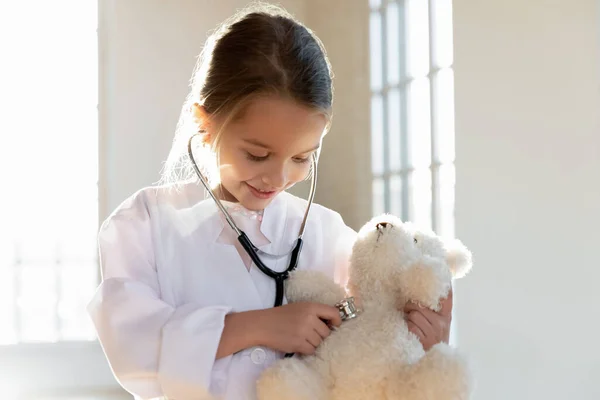 Lachend schattig klein meisje draagt witte jas, met behulp van stethoscoop. — Stockfoto