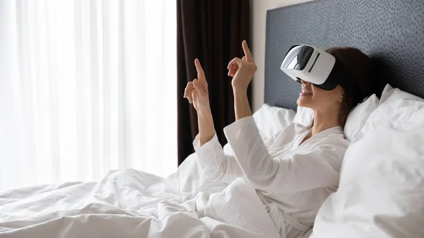 Sorridente giovane donna che indossa occhiali di realtà virtuale, dispositivo di test a letto . — Foto Stock