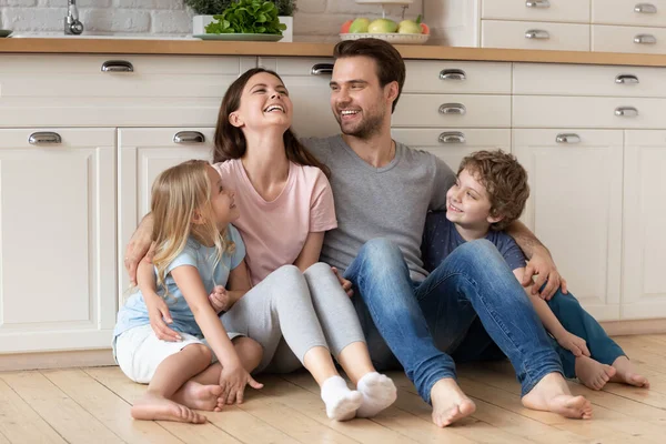 Glückliche junge Eltern sitzen mit kleinen Kindern auf dem Boden — Stockfoto