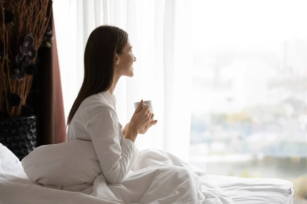 Wanita bahagia duduk di tempat tidur dengan secangkir kopi . — Stok Foto