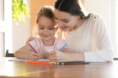 Genç anne mutlu küçük kızın omuzlarını kucaklıyor, resimler çiziyor..