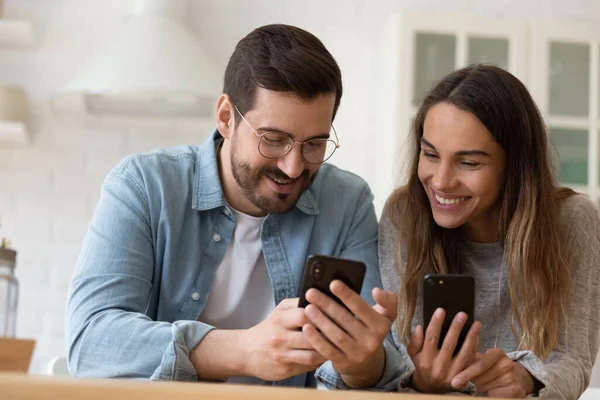 Happy young couple using smartphones together, having fun