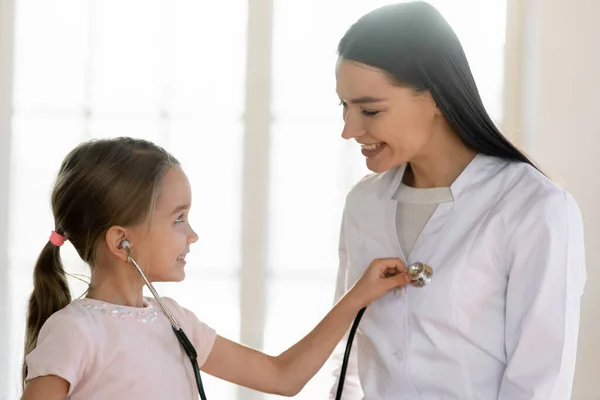 Kleine süße Patientin trägt Phonendoskop, hört Herzschlag der Krankenschwester. — Stockfoto