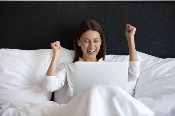 兴奋的年轻女人看着手提电脑屏幕，在床上放松. — 图库照片