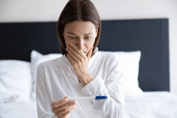 Geschokt brunette vrouw kijken naar plastic zwangerschapstest. — Stockfoto