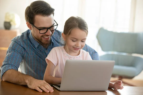 Молодой отец обнимает маленькую дочку, используя компьютер . — стоковое фото