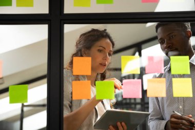 Mentor Afrikalı Amerikalı stajyere çıkartmalarla ilgili proje planını anlatıyor.