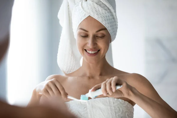 Smiling woman with towel on head doing morning toothcare routine. — Stock Photo, Image