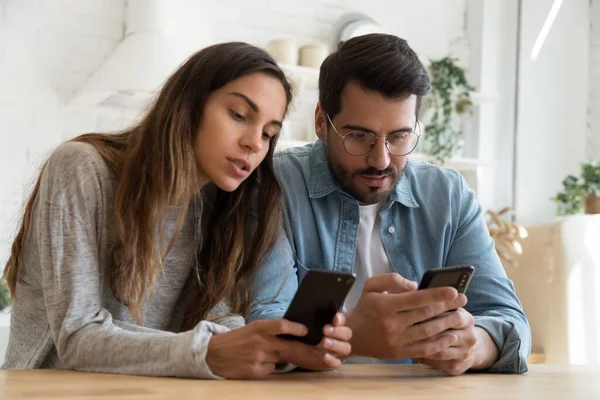 Young couple using smartphones, discussing news, looking at screen