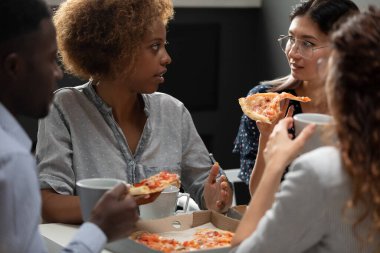 Çeşitli meslektaşlar birlikte pizza yiyor, öğle arasında sohbet ediyorlar.