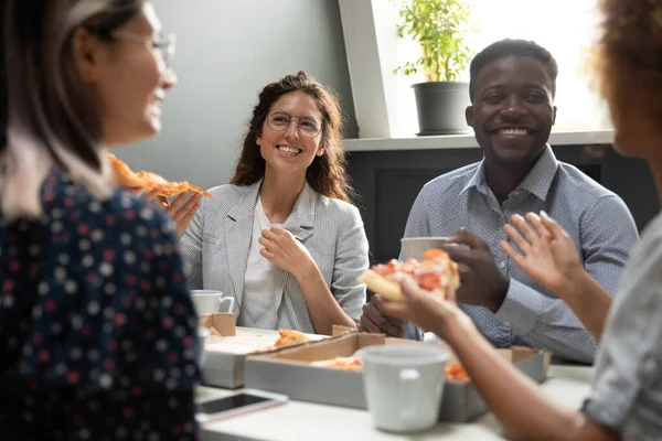 Felices colegas diversos sabroso comer pizza, charlando durante la pausa para el almuerzo — Foto de Stock