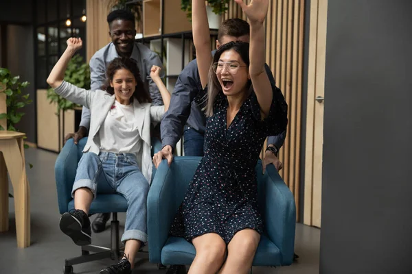 Spännande affärskvinnor rider på stolar, diverse kollegor har kul — Stockfoto