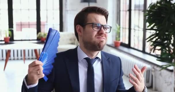 Unhappy exhausted businessman wearing suit waving fan in office — Stock Video