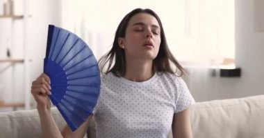 Mutsuz genç bir kadın yelpaze sallıyor. Evde kendini rahatsız hissediyor.