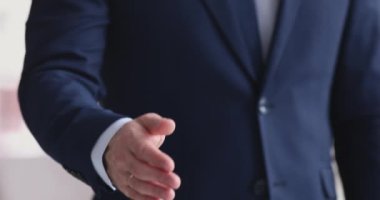 Takım elbiseli bir iş adamı el sıkışmak için kameraya uzanıyor.