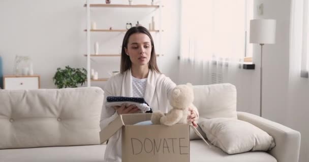 Счастливая женщина-волонтер упаковывает детскую донорскую коробку, глядя в камеру — стоковое видео